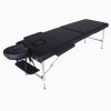 An unfolded 2-section black vinyl portable massage table with a sturdy, polished stainless steel frame. Features include a removable U-shaped face cushion, a hanging arm shelf, and removable padded side armrests, shown in an elevated three-quarter view.