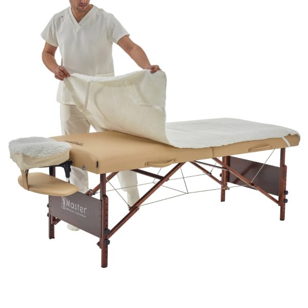 Massage therapist in cream scrubs unfurling a soft white fleece table cover onto a Master massage table.