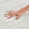Macro shot of a hand pressing into a deeply piled white fleece massage table pad, showcasing its fluffy and insulating quality.