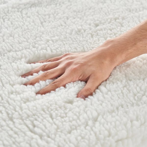 Macro shot of a hand pressing into a deeply piled white fleece massage table pad, showcasing its fluffy and insulating quality.