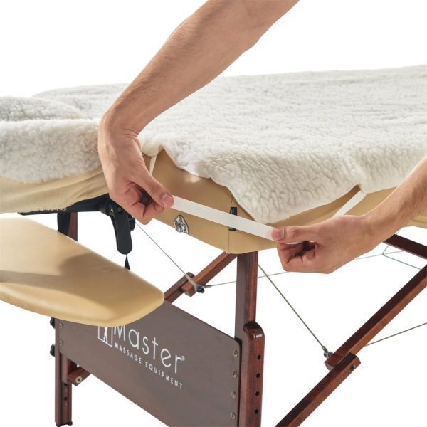 A massage therapist's hands stretching the elastic corner band of a white fleece table cover to secure it to a portable table.