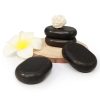 Premium hand-polished black basalt hot stones stacked on a wooden plate next to a white frangipani spa flower.
