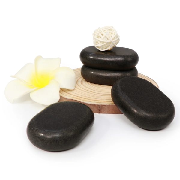 Premium hand-polished black basalt hot stones stacked on a wooden plate next to a white frangipani spa flower.
