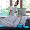 A side view of a client lying on a black massage table, holding a remote control while the table's blue illuminated airbags provide active stretching along their back.