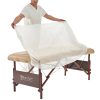 Therapist draping a disposable white fitted cover over a beige massage table.