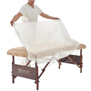 Therapist draping a disposable white fitted cover over a beige massage table.