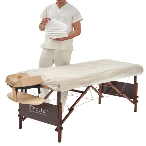 Therapist draping a disposable white fitted cover over a beige massage table.